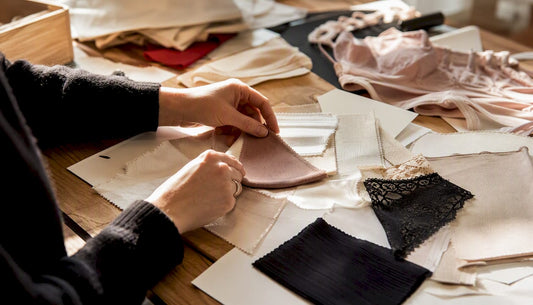 Des mains qui effleurent différents échantillons de tissus de lingerie, appréciant la douceur et la finesse des matières.
